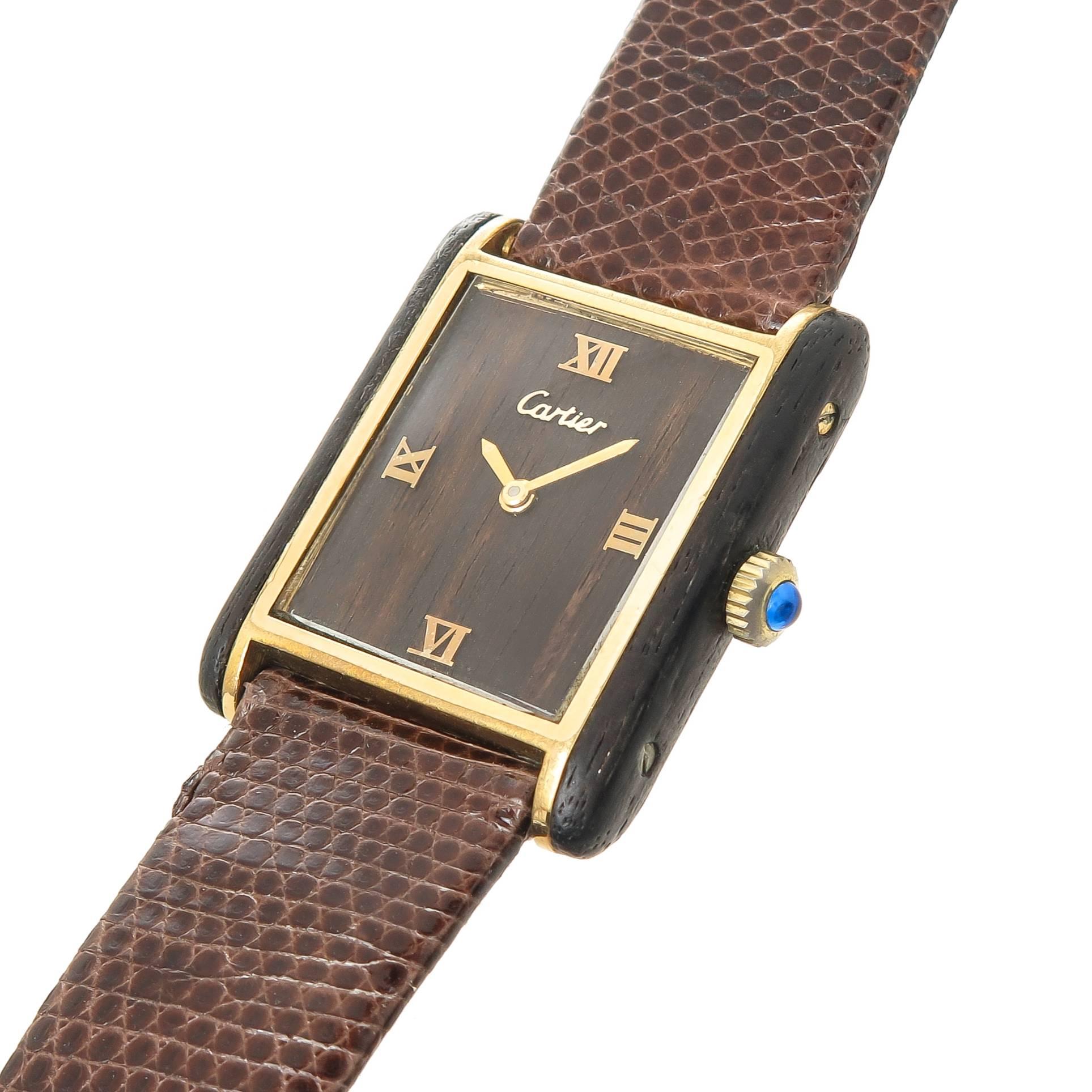 Circa 1970s Cartier Wood Tank Watch. 33 X 25 MM Gold Plate Case with Mahogany Wood Sides. 17 Jewel mechanical, Manual wind movement, Mahogany wood dial with raised Gold Markers. Sapphire Crown. New Brown Lizard strap with original Cartier Gold plate