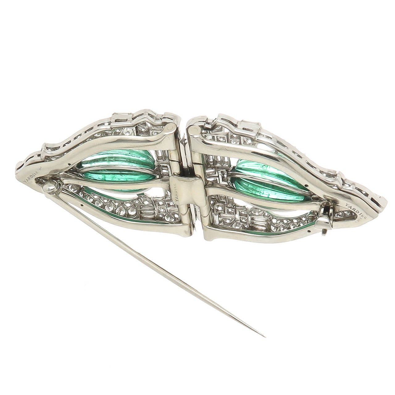 Circa 1930s Dress Clips By Raymond Yard, Platinum, Round, Marquise and Baguette Diamonds totaling 6 Carats. Further set with 2 Oval Ribbed cut Emeralds. totaling approximately 12 Carats. This Piece has its original Backing to be worn as a single