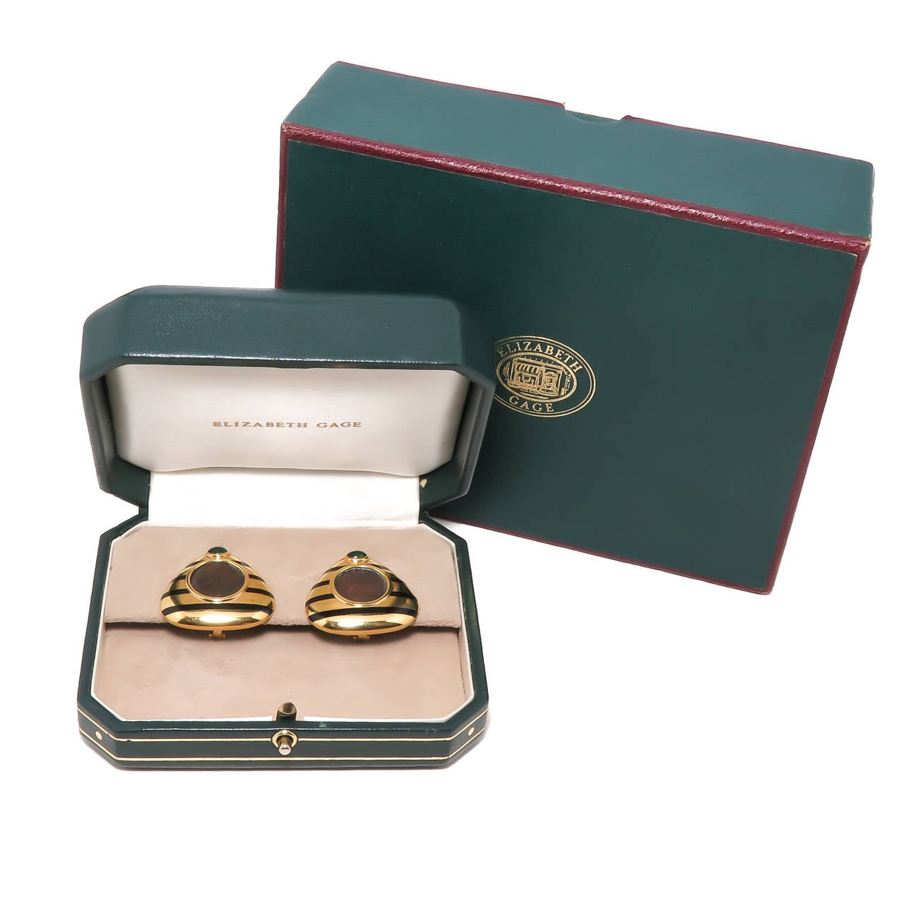 Circa 2000 Elizabeth Gage 18K Yellow Gold Earrings, centrally set with ancient Bronze Coins, further set with Cabochon Emeralds and having Black Enamel. Clip backs to which a post can be easily added. Measuring 1 1/4  X  1 5/16 inch in length.