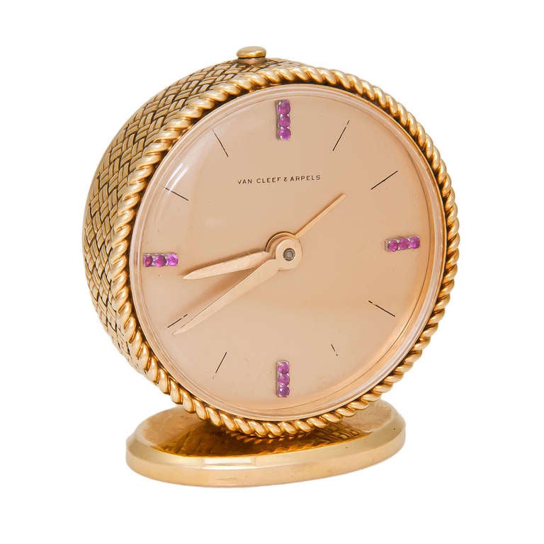 Van Cleef & Arpels 18k yellow gold alarm clock, circa 1960s. Woven and twisted rope design sides and bezel. The dial is set with ruby indexes at 3, 6 and 9 o'clock. Manual-wind movement with alarm function. Signed and numbered.