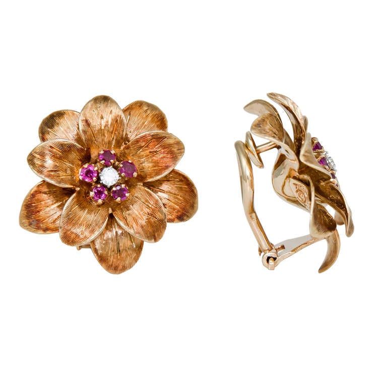 Circa: 1960s Tiffany & Company 18K Yellow Gold and Gem set Flower Form Ear Clips. Texture finished Petals and centrally set with a Round Brilliant cut Diamond and Surrounded by Rubies. Omega Clips. A post can be easily added.