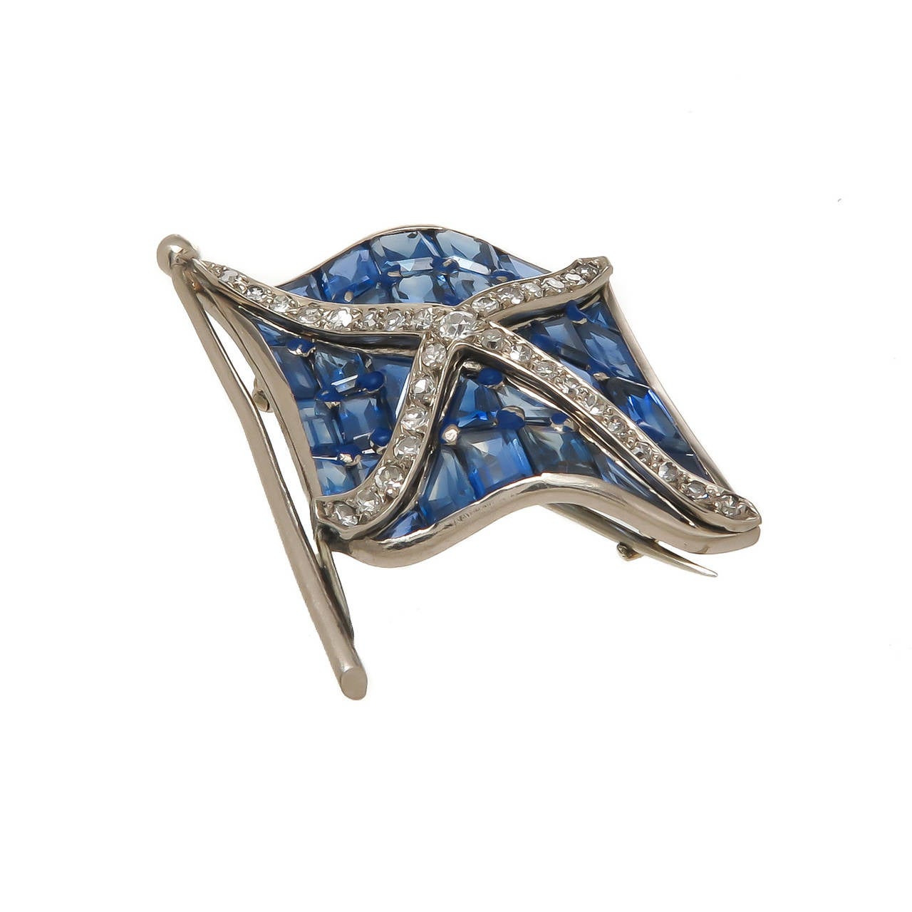 Circa 1930 Platinum Diamond and Sapphire waving Flag Brooch. Set with step cut Sapphires of Ceylon Color and Origin and an X in the center set with old cut Diamonds. Measuring 1 1/2 inch in length and 1 inch wide.