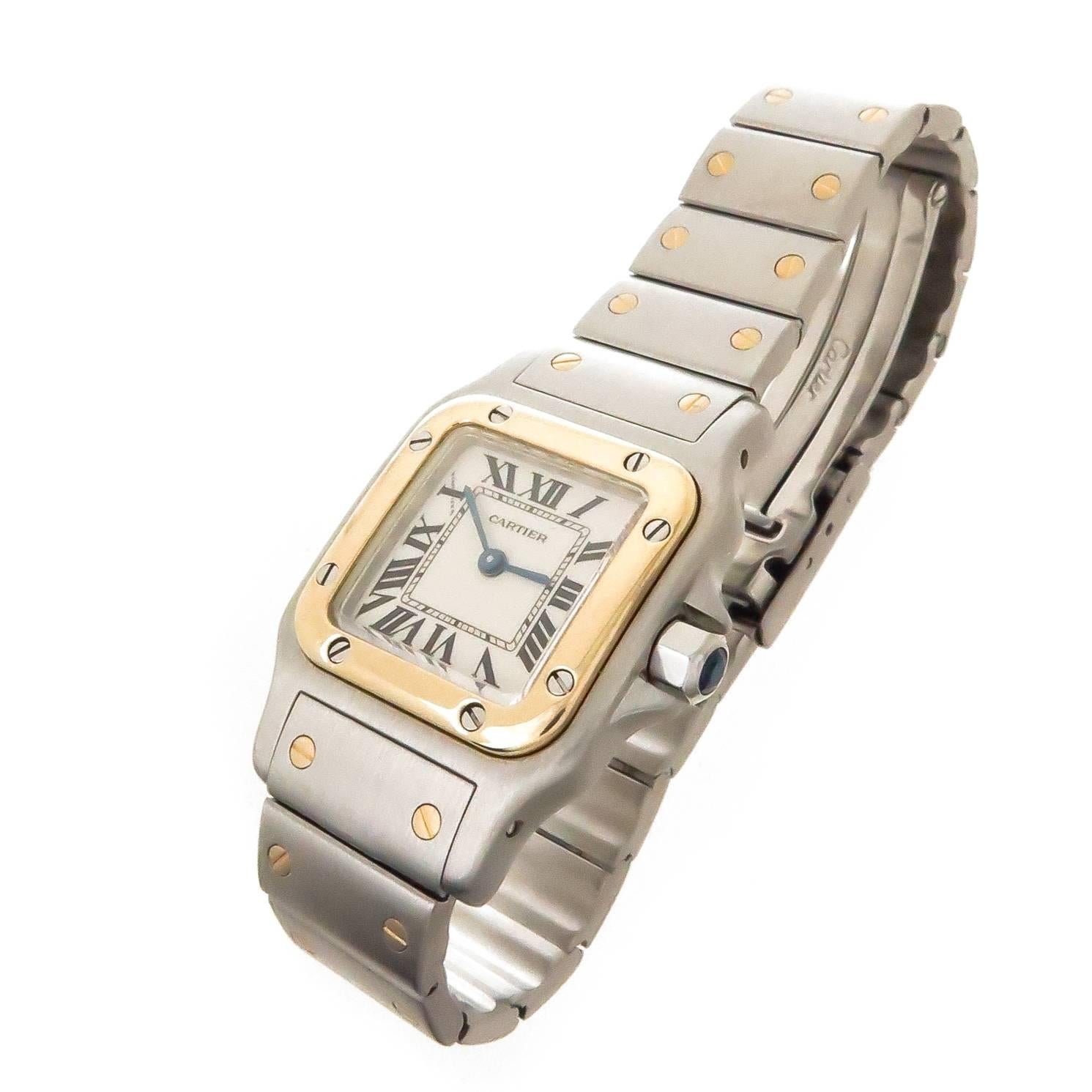 Circa 2000 Cartier Santos Ladies Wrist watch, 35 X 33 MM Stainless Steel and 18K Yellow Gold Water Resistant case. Quartz Movement, White Dial with Black Roman Numerals and a Sapphire Crown. 1/2 inch wide Steel and 18K bracelet with Deployment