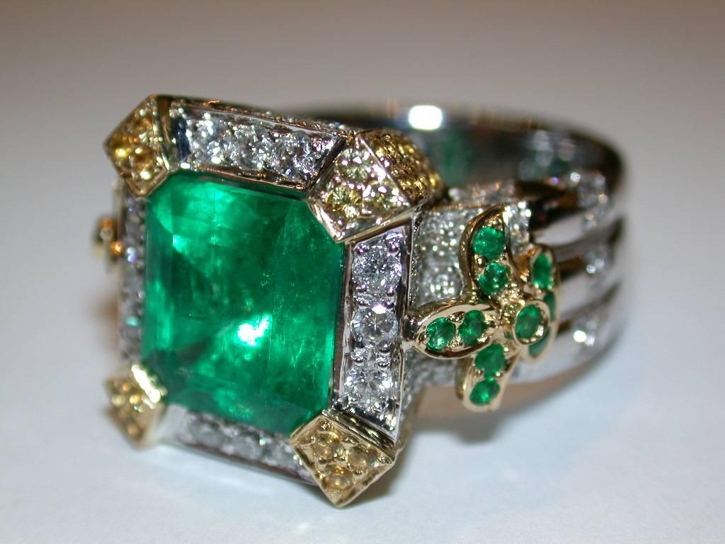 Custom, handmade emerald ring designed by Erin MacGeraghty. The emerald is over 5cts and is a gorgeous green color surrounded by 1ct of pave round white diamonds, G, VS2 and yellow sapphires with prong set emeralds set in the Fleur de lys prongs. 