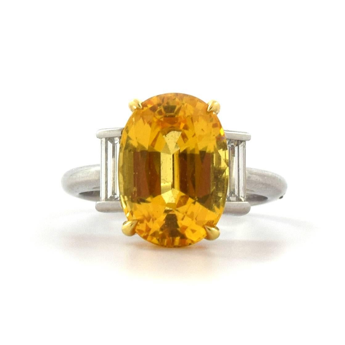 This Tiffany & Co ring is definitely a beauty. The ring is accented by two long baguette diamonds. the center stone is a lively oval shaped Yellow Sapphire weighing 7.42 carats graded by the American Gemological Laboratories (AGL) as unheated
