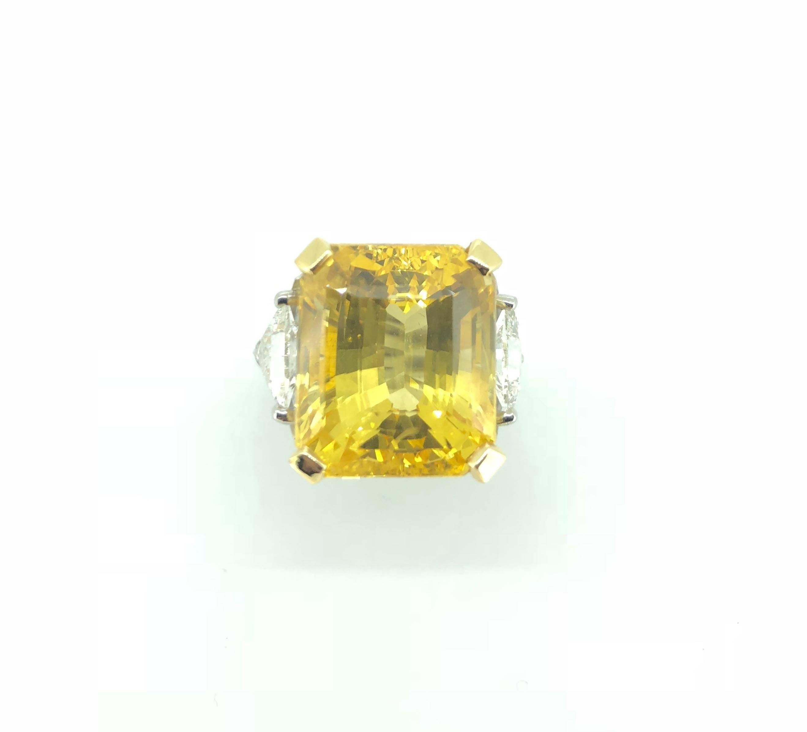 A Vivid Natural Yellow Sapphire Emerald Cut 20.01 Carats Mounted in 18K Yellow Gold and Platinum Ring. 

The Central Emerald Cut Yellow Sapphire is flanked by two Triangle-cut diamonds total 0.98 Carats, sweeping gracefully either side by round