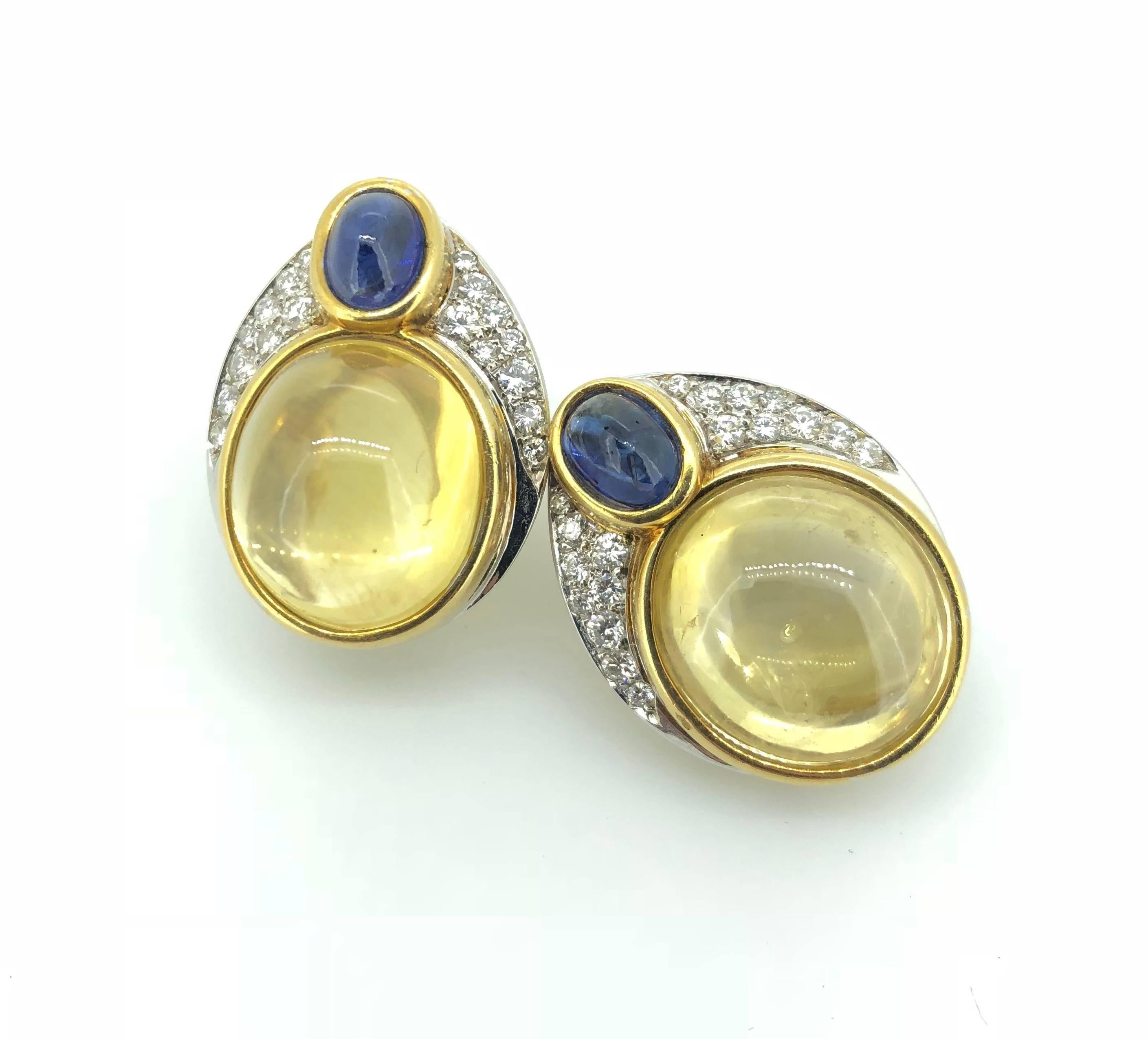 Retro Period 14 Karat Gold Yellow Sapphire Cabochon (Circa 45 Carats) Diamond And Blue Sapphire Cabochon Ear Clips. 

The Yellow Sapphire Cabochons enveloped by rub-over setting and accented with blue sapphire cabochon and round brilliant cut white