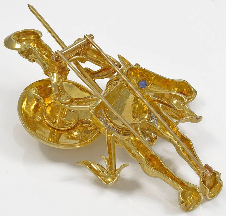18 karat gold pin representing Cervantes' Don Quixote on his horse, with a diamond collar, ruby nose and sapphire eyes. The shield is embossed with diamonds and blue enamel.