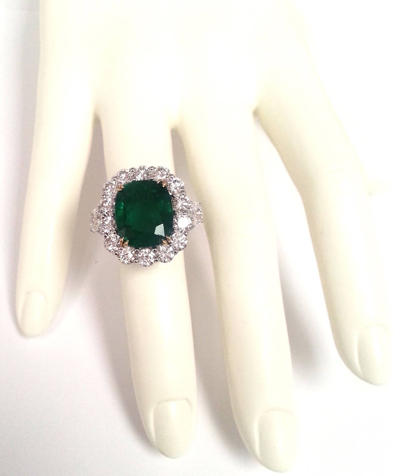 Hand made Platinum ring featuring a diamond halo of large stones and two oval diamonds as side stones. The center emerald has an ideal emerald color of deep green shade and it weights 8.62ct t.w. The total diamond carat weight of the ring is