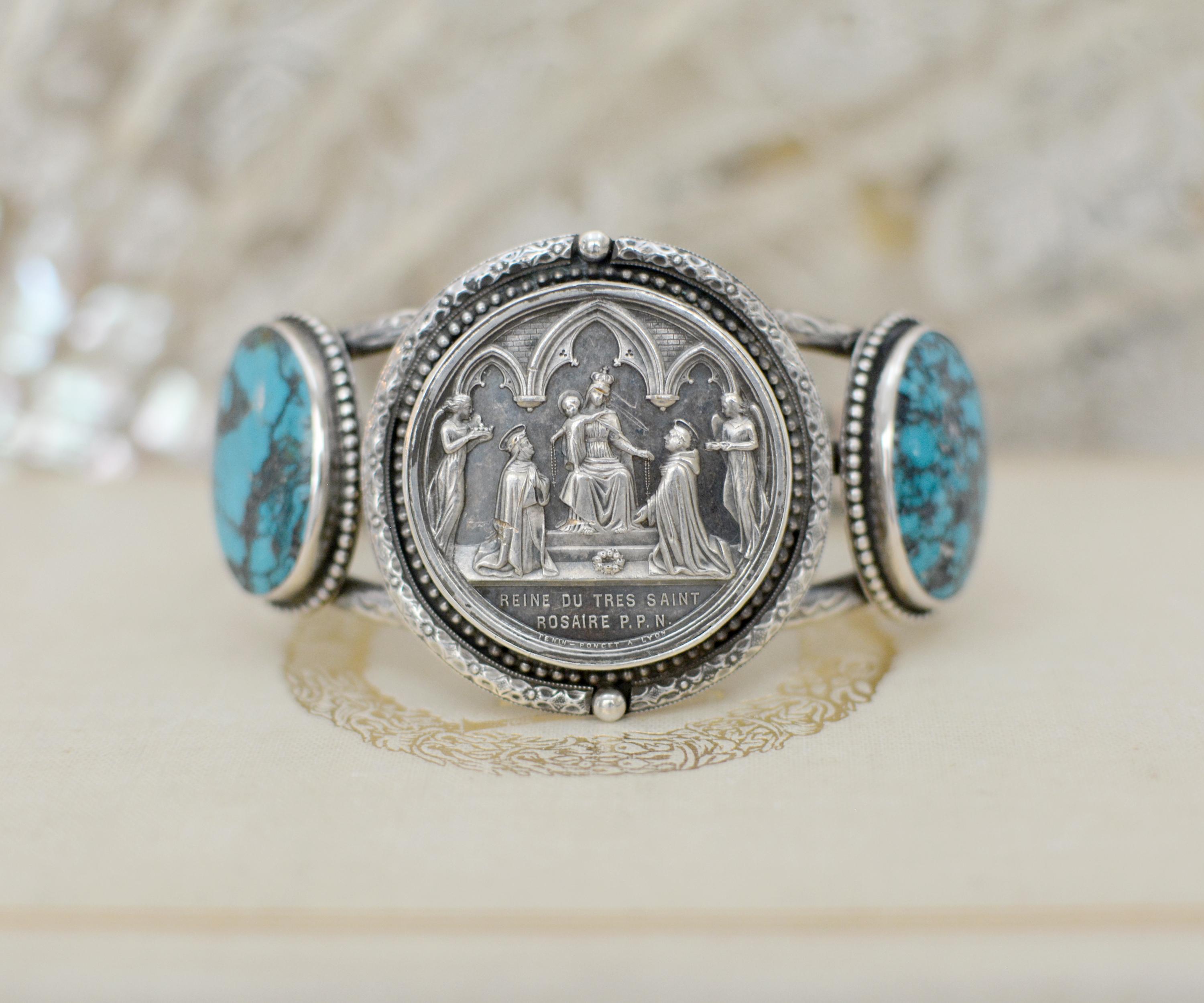 Dieses einzigartige Manschettenarmband aus Sterlingsilber zeigt eine originale antike französische Heiratsmedaille aus dem neunzehnten Jahrhundert, die die Mutter Maria mit dem Jesuskind an ihrer Seite darstellt. Unter dem knienden Paar stehen die