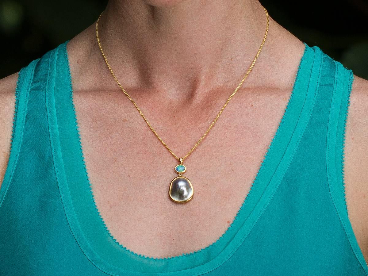 A glowing Perlas del Mar de Cortez Mabe Pearl meets its match with a Hopkins Australian Lightening Ridge Opal in this pendant with hammered 22 and 18 karat reclaimed gold. The bail is accented with a VS Canadian diamond. Accompanied by a 18 karat
