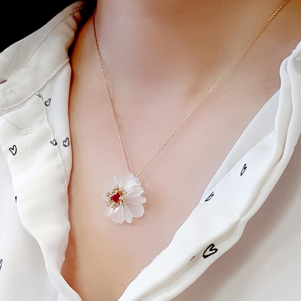 Ce ravissant pendentif floral en or présente une fleur translucide aux pétales sculptés, centrée sur un rubis vif entouré d'un halo de pierres blanches étincelantes. Délicat équilibre entre élégance et fantaisie, il apporte une touche romantique à