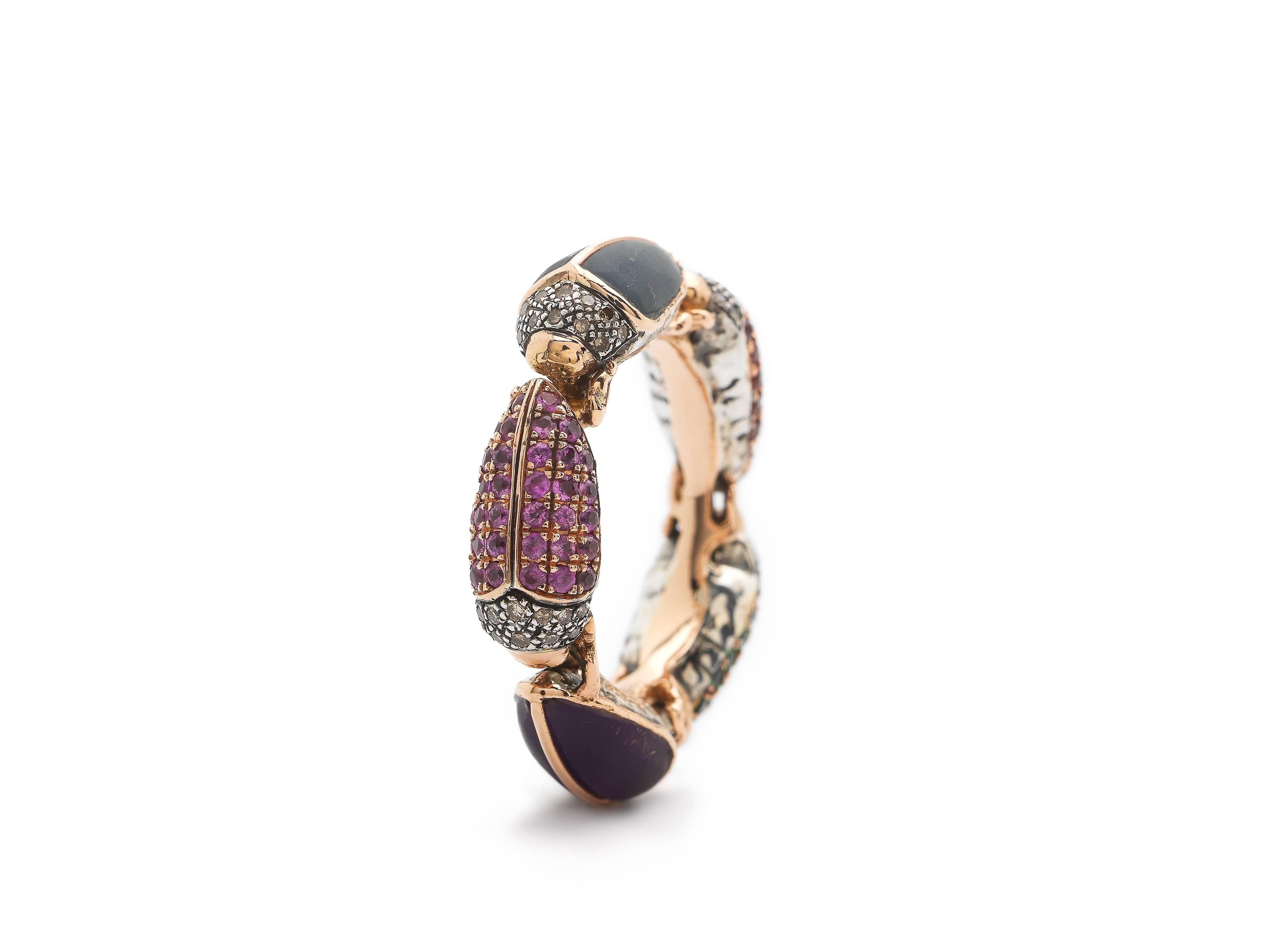The Scarab Eternity Ring from Bibi van der Velden features a row of small scarabs lined up head-to-tail, in various gemstone tones and materials. The ring is composed of 18k Rose Gold, with Sterling Silver scarabs, set with diamonds on their heads.