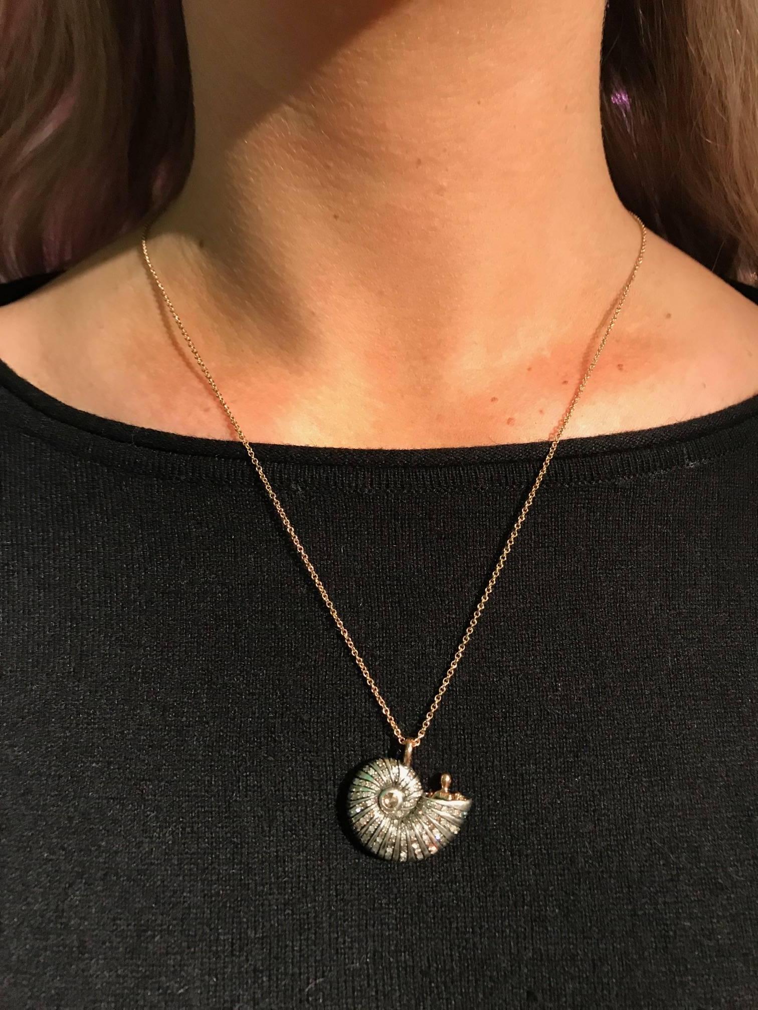 The 'Poseidon's Getaway' Necklace by Bibi van der Velden, includes a Sterling Silver shell, set with brown diamonds, rose cut diamonds, and blue and green shades of sapphires. It includes an 18k rose gold man peeking out of the spiral shell, his