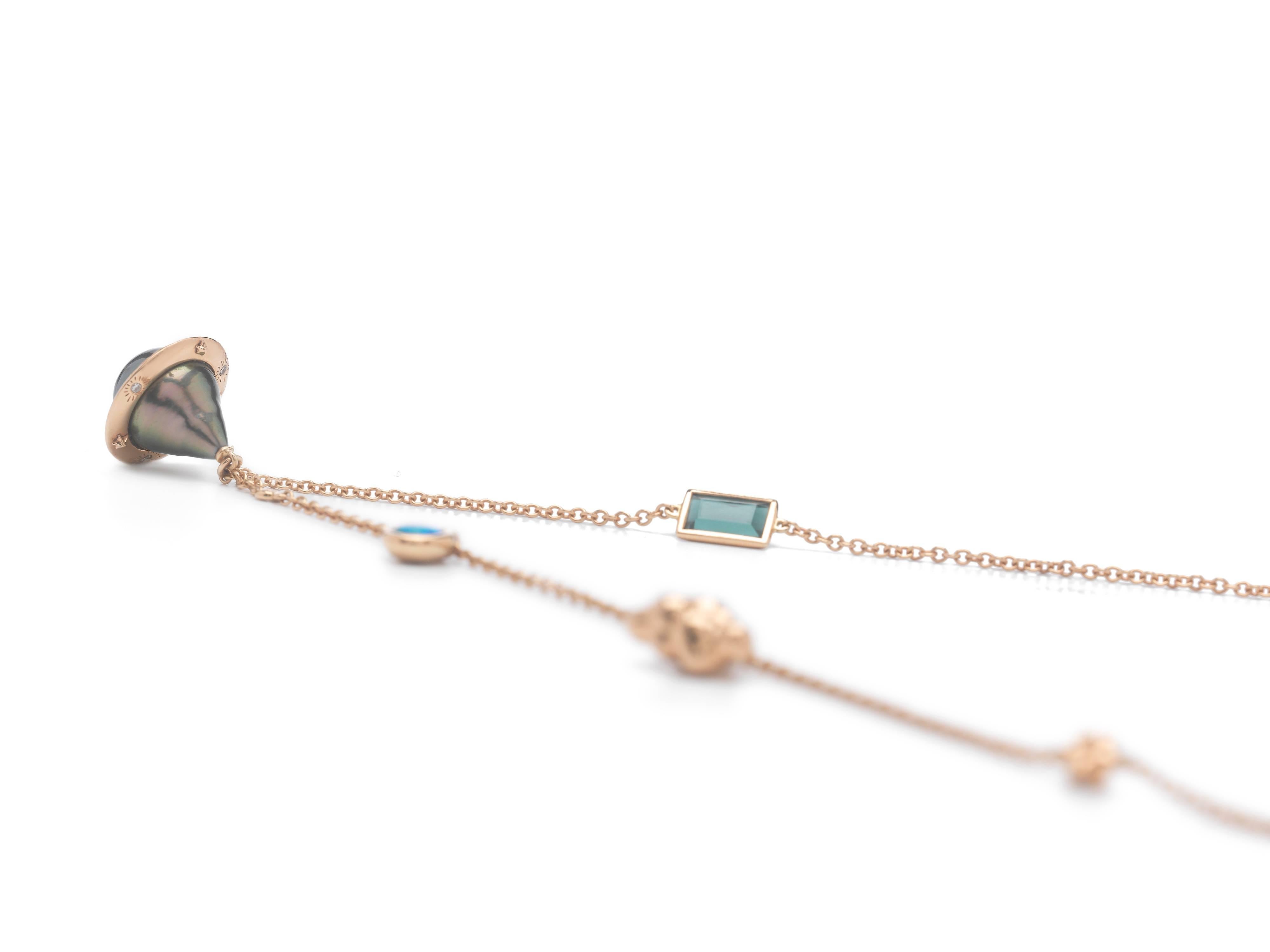 The Small Planet Necklace, by Bibi van der Velden, is made of 18k Rose Gold, and features a Tahitian drop pearl, wrapped by a gold planet ring set with diamonds and blue sapphires. The necklace chain features a tourmaline, opal, and 18k stars and