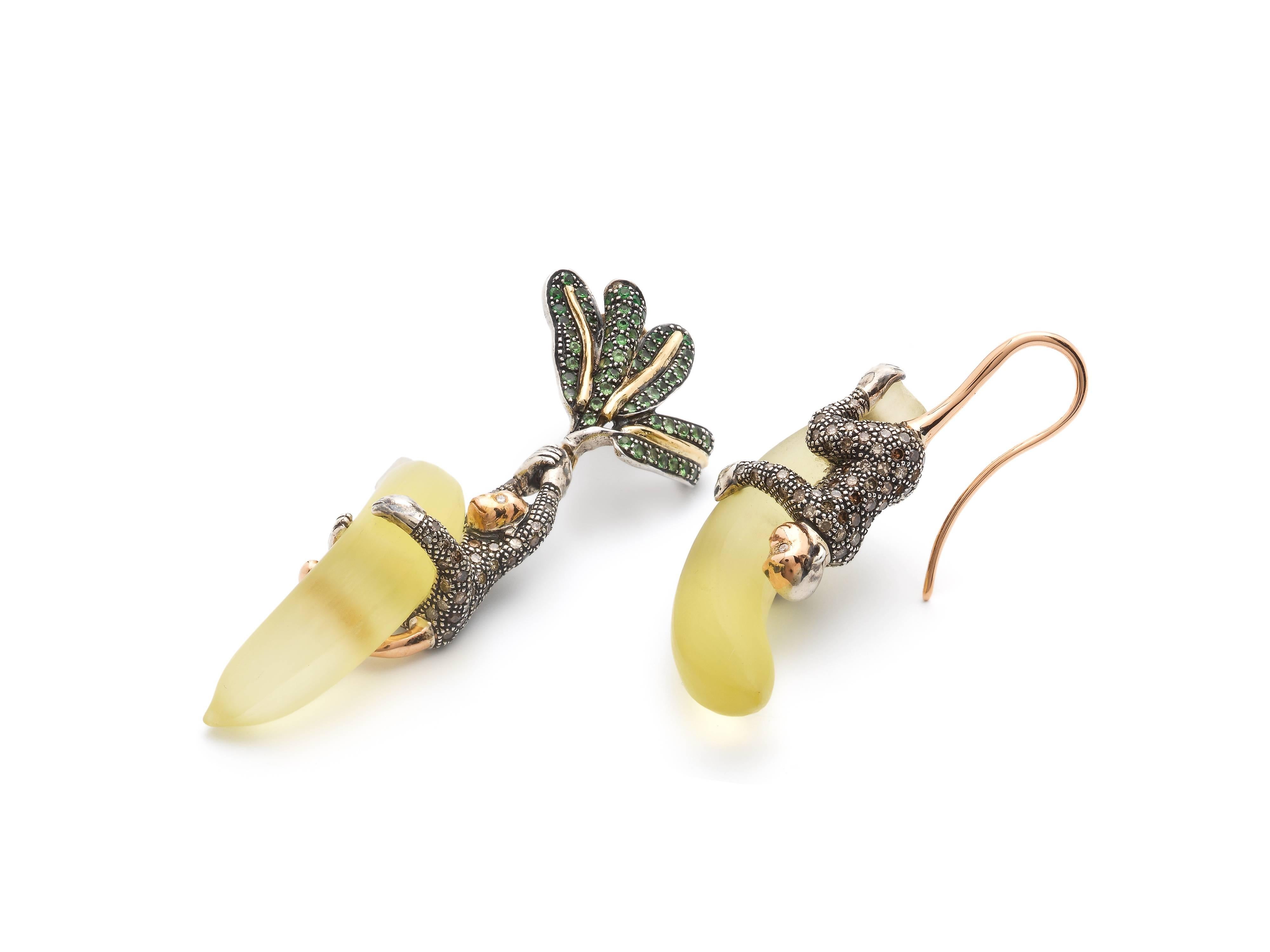 These fun, asymmetrical earrings show two monkeys made of 18k rose gold and sterling silver. Set with brown and white diamonds, they hold on tight to their hand-carved lemon quartz bananas. The palm leafs are embellished with vivid green Tsavorites