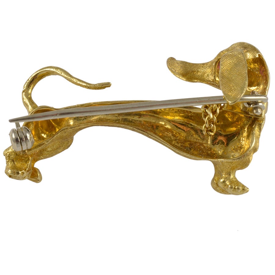Adorable figural dachshund pin. Made and signed by Cartier. 
Textured 14K yellow gold with bright faceted ruby eye.
Tail up and head turned around, looking for her owner.
1 1/2