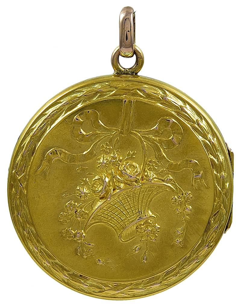 Very fine and exceptionally lovely round gold hinged locket.   Embossed basket of flowers, with a flowing ribbon; applied reed and ribbon border.  Reverse side has same reed and ribbon border, surrounding the original beveled glass.  1 1/4