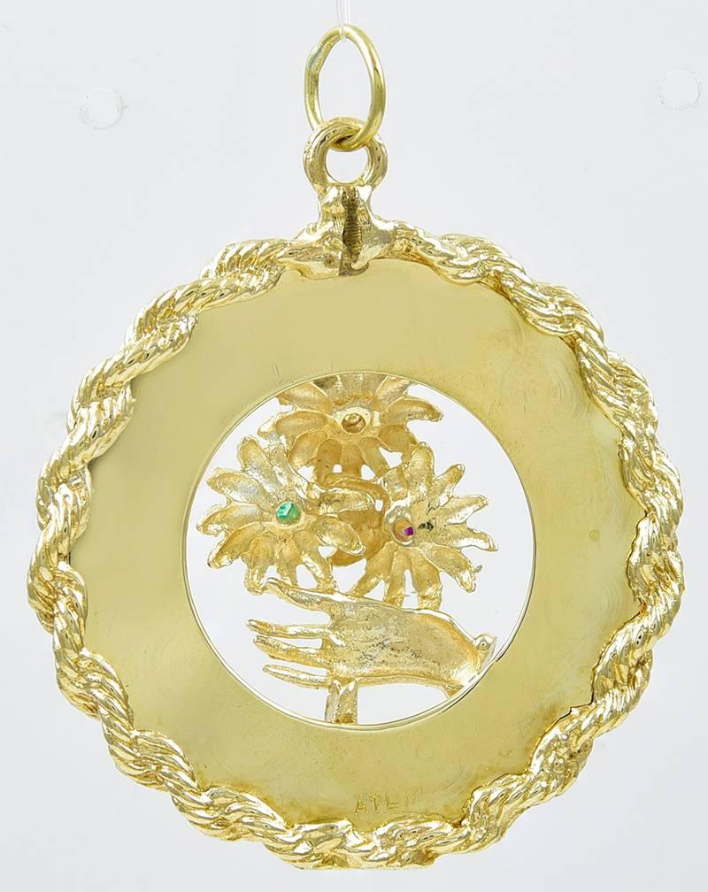 Large charm, with engine-turned panel engraved "To Mother" surrounding a figural hand offering three flowers.  The flowers are set with a diamond, an emerald and a ruby.  Applied rope twist border.  14K yellow gold.  1 3/8" in 