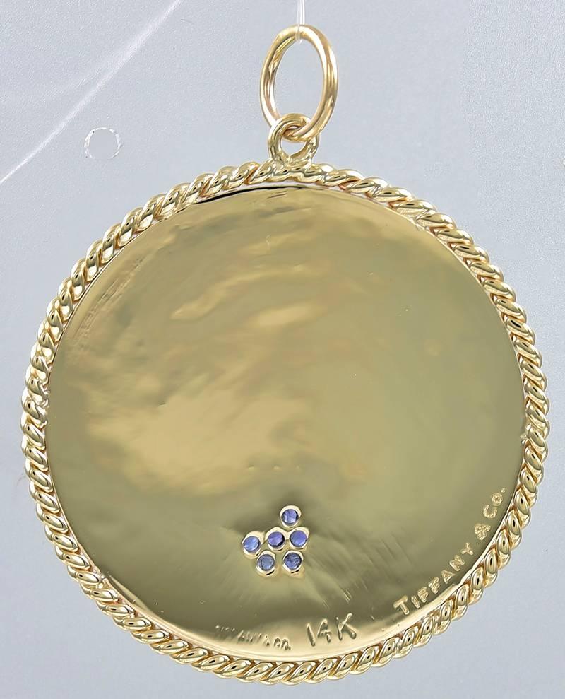 Large charm, made and signed by TIFFANY & CO.  Round disc with a deeply engraved radiating line pattern.  Rope twist border.  Set with an asymmetrical
applied heart, with faceted sapphires.  1 1/3