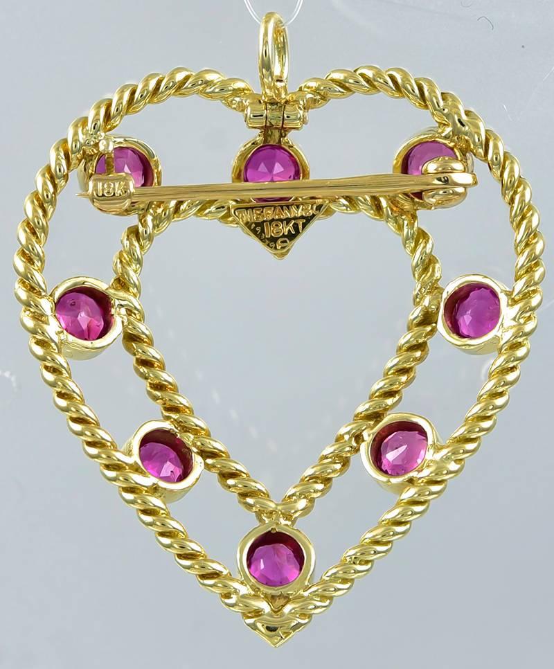 Beautiful double-heart pendant.  Made and signed by TIFFANY & CO.
Eight bright faceted rubies are set between the two hearts.  18K yellow gold, in a rope twist pattern.   Very well made, with the pin hidden behind the inner heart  and the bail that