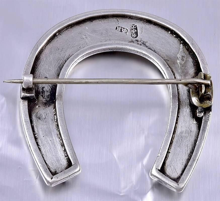 Antique sterling silver figural horse-shoe pin with inlaid multi-color enamel letters in Russian (Old "Slavonic"), saying "Wear With Happiness."  1 2/3" x 1 2/3."
An endearing piece of antique jewelry.

Alice Kwartler