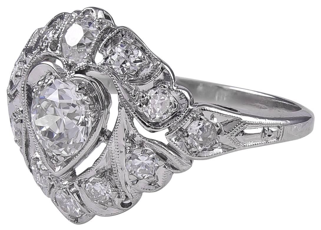 Beautiful antique diamond engagement ring: the center stone is .70 ct., set in an openwork heart-shaped reserve.  G-H color.   Surrounded by .55 cts. of smaller brilliant diamonds, G-H color, VS-SI1.  Set in a platinum mounting, with fine milgrain