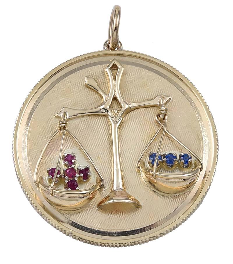 Large charm, with applied "Libra" symbol, suspending two baskets, one with a plus sign set with rubies and one with a minus sign set with sapphires.  Matte 14K yellow gold, with cut coin edge.  The back is engraved "I Love You More