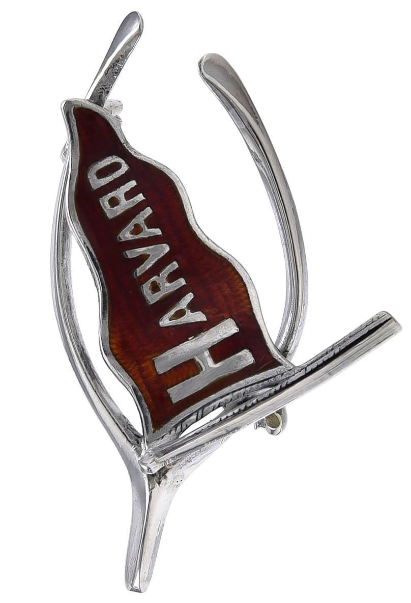 Sterling silver pin.  A banner, with red enamel background, that spells "HARVARD."  Superimposed on a sterling wishbone.  1 1/3" x 3/4."  

Alice Kwartler has sold the finest antique gold and diamond jewelry and silver for over