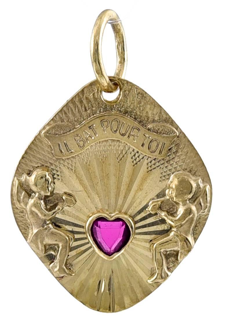 Most charming charm:  shield-shaped, with textured gold background.  In the center is an applied ruby heart surrounded by two cherubs.  An applied banner on top says "IL BAT POUR TOI" -- " IT BEATS FOR YOU."  18K yellow gold. 