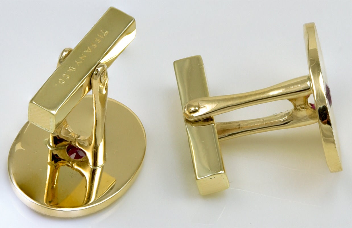 Large oval cufflinks, made and signed by Tiffany & Co. Deeply engraved radiating line pattern, set with a large faceted ruby. 14K yellow gold. 7/8