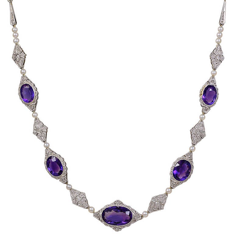 Antique necklace set with 5 oval faceted amethysts surrounded by diamonds. Each link is separated with a pearl. The amethysts and pearl are separated by diamond shaped filigree links set with small diamonds.
The total carat weight of the amethysts