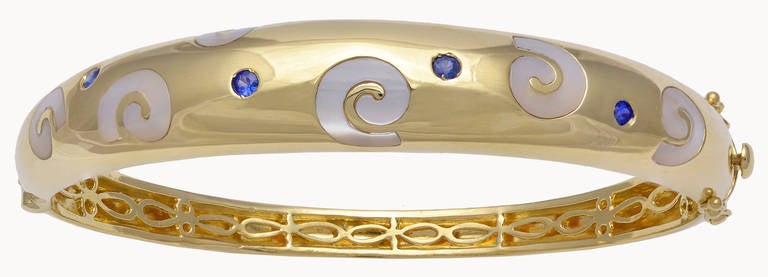 Unique 18k yellow gold bangle bracelet. Inlaid with geometric mother -of- pearl motifs, set with faceted sapphires. Hugs the wrist. Beautifully made. 
A very attractive, distinctive  bracelet with a moderne flare.
