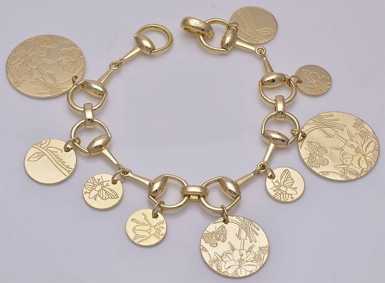 Fabulous Horse-bit charm bracelet made and signed by Gucci. Signature Gucci 18K gold link bracelet set with round charms, beautifully engraved with butterflies and Irises from the Floral Collection. All engraving accented with fine white enamel