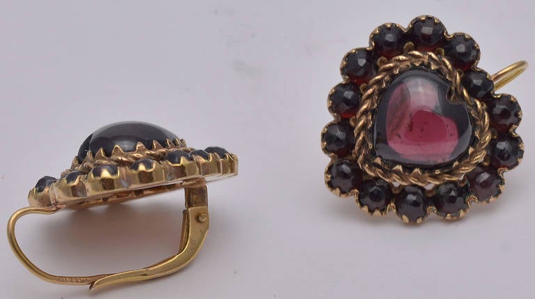 Beautiful antique heart shaped earrings in bohemian garnet. Large beautifully rounded center stone surrounded by smaller cabochon garnets. Set in garnet gold with14K gold wires. A very feminine and beautiful earring. Made circa 1900.