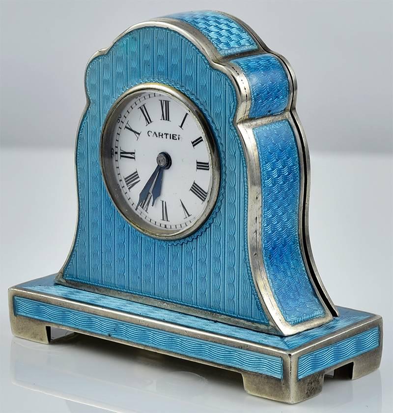 Beautiful enamel and sterling silver miniature mantel clock. Made and signed by Cartier. All over teal blue guilloche enamel. White dial with Roman numerals. Mechanical. Very graceful form. 1-1/2