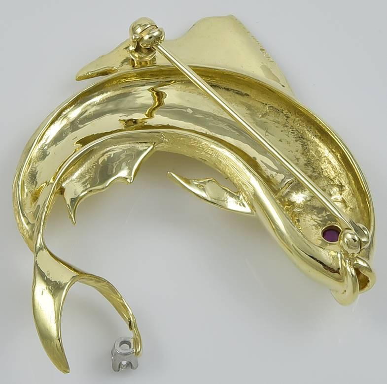 Figural leaping fish brooch. Signed by Cellino. Very realistic. Shining and iridescent 18K gold finish. Cabochon ruby eye; faceted diamond set in tail. 1-1/3