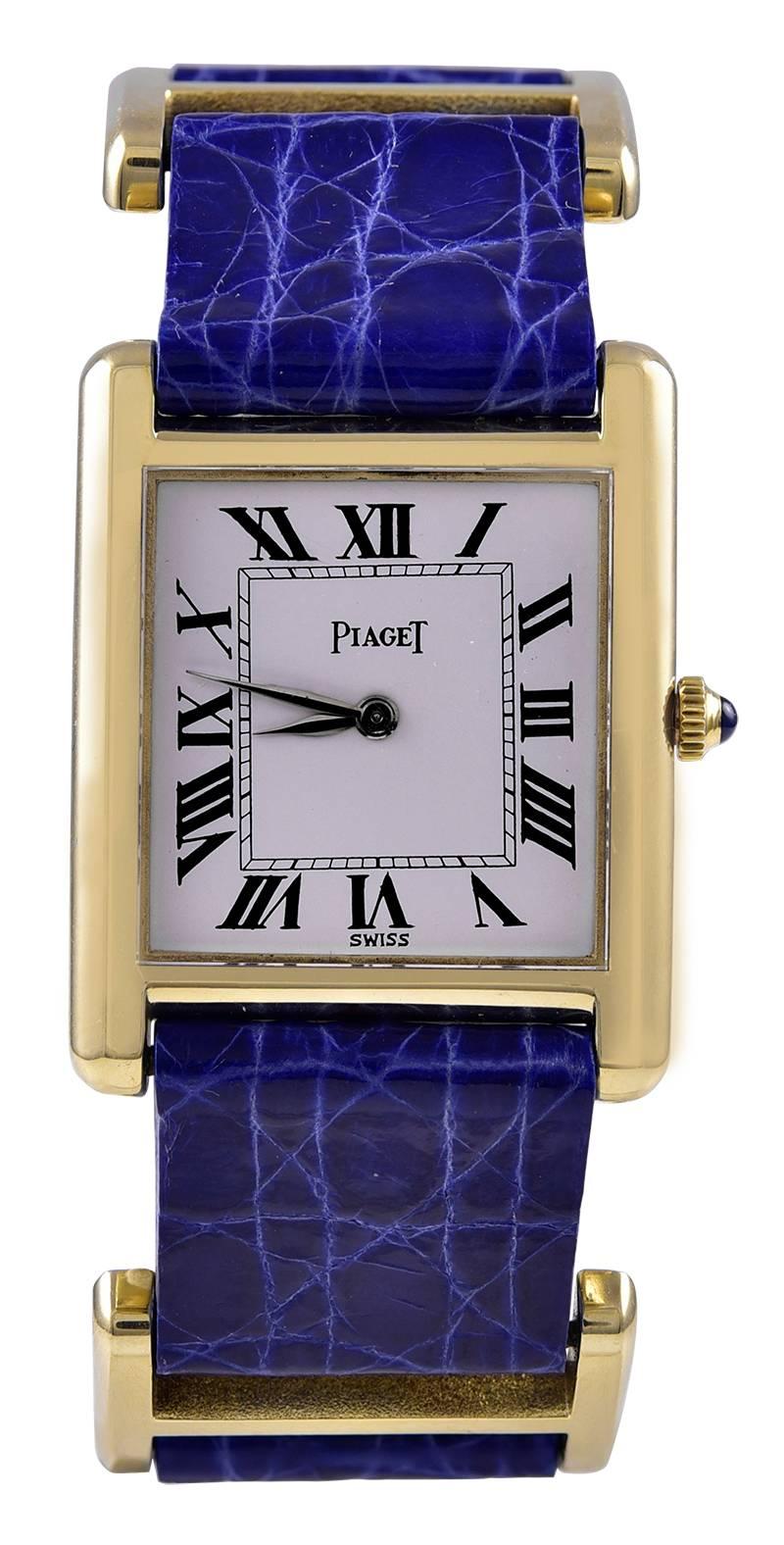 Slim and sleek true tank watch.  Made and signed by PIAGET.  18K yellow gold, with double bar bands between the watch and the buckle.  Mechanical movement.  Roman numerals. Navy crocodile band.  Streamlined to the wrist; a fabulous wrap-around look.