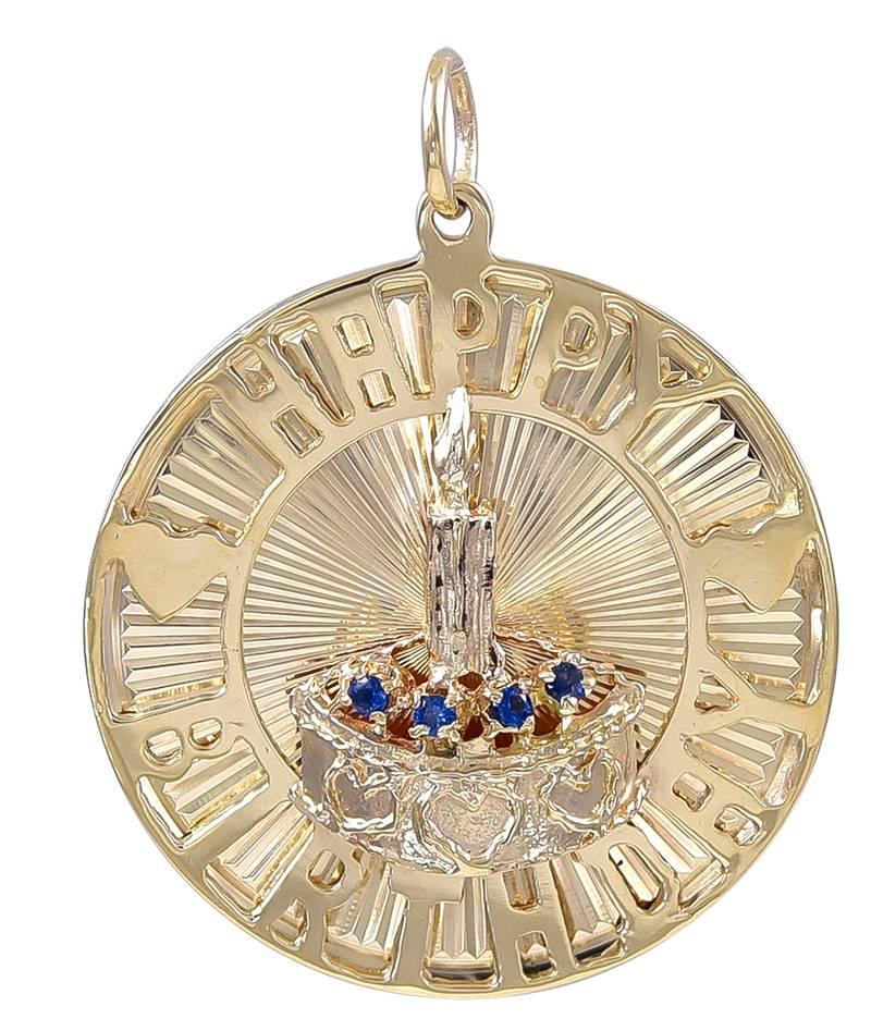 Large round charm.  The border is mounted with applied letters that spell out "Happy Birthday" separated by two gold hearts.  In the center is a three-dimensional birthday cake, set with four sapphires, and a candle.  The entire charm is