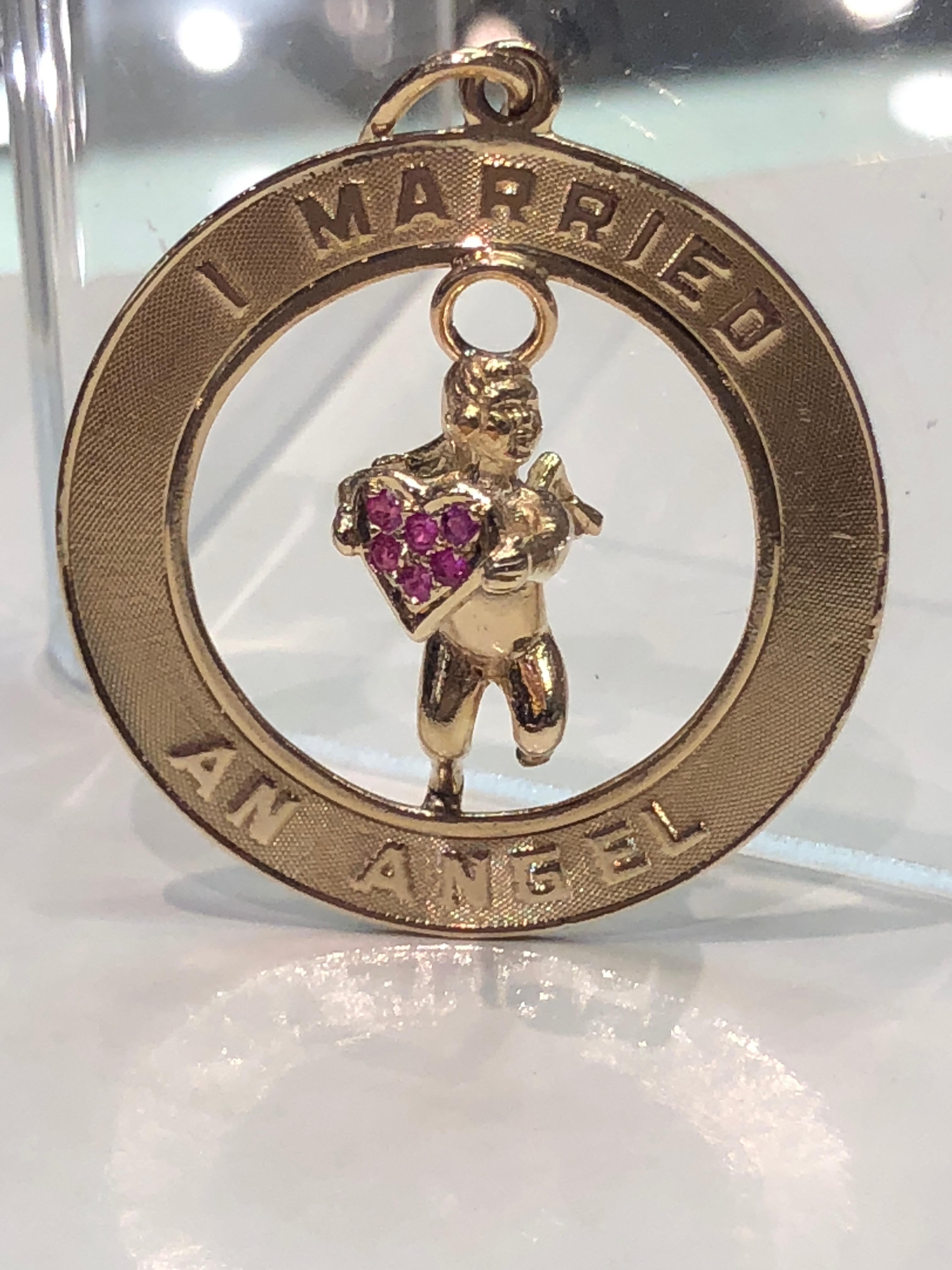 Large 14K gold pendant/charm. Figural cherub holding a ruby-encrusted heart.  Engraved around the border:  
