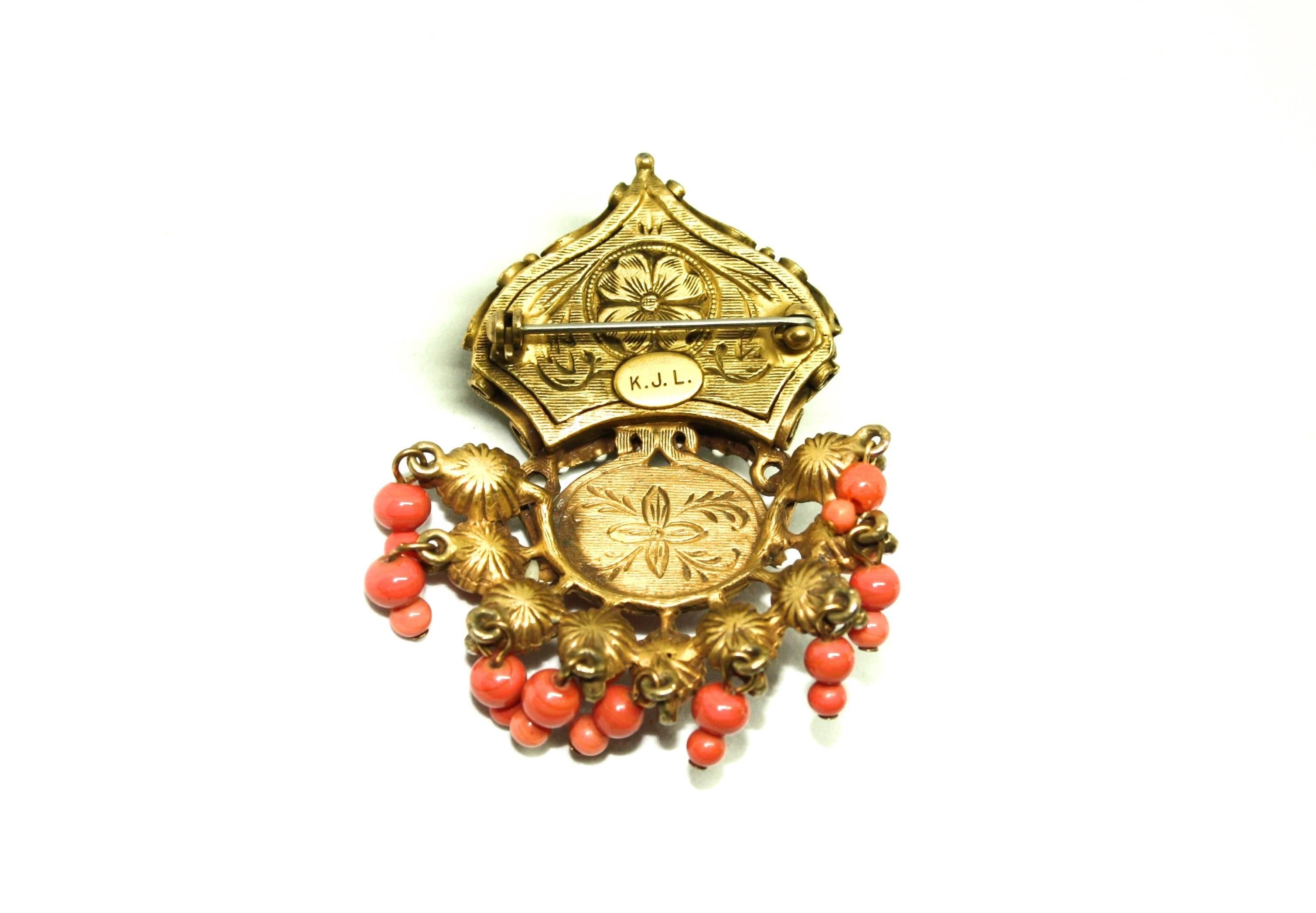 Gorgeous coral colour stones on antiqued metal featuring white enamel accents. This brooch also features articulated drop coral colour beads and is extremely detailed, even on the reverse! It is one of Ken Lane's earliest pieces, featuring the K.J.L