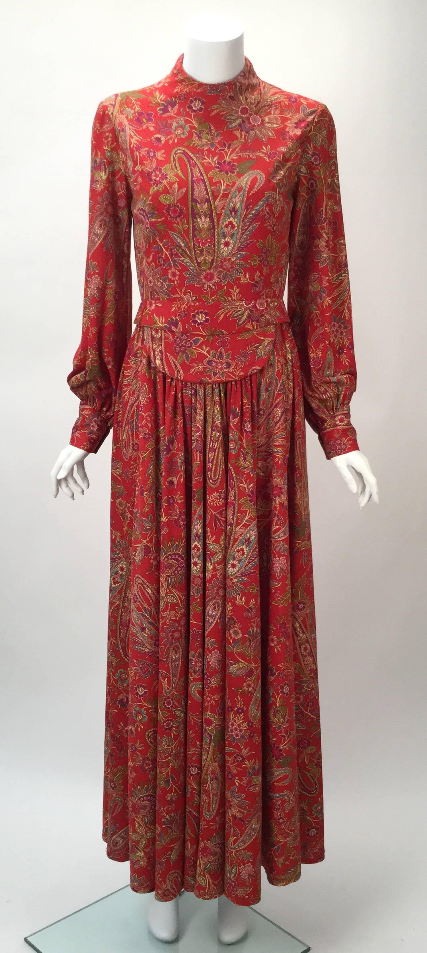 This 1960's Shannon Rodgers for Jerry Silverman maxi dress features a high neck and bishop sleeves. Front bib design detail. Bodice is lined.  Soft pleating falls from waist. Zipper running center back. Belt in the same paisley print. The ends are