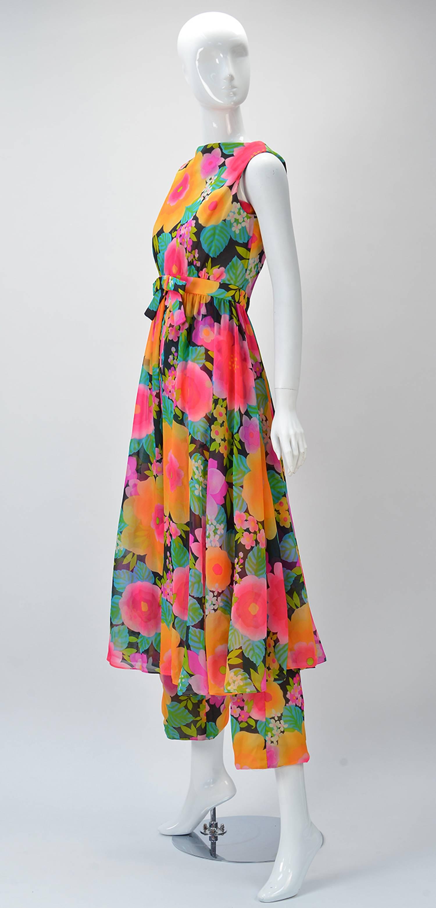 Wonderful 1960's Pat Sandler Floral Jumpsuit and Overdress solid the exclusive Silver Key shop of Neiman Marcus in the 1960's. 

The ensemble follows a fantastic bright floral print. Defined waist with gathering. Center bow on waistline. Zipper