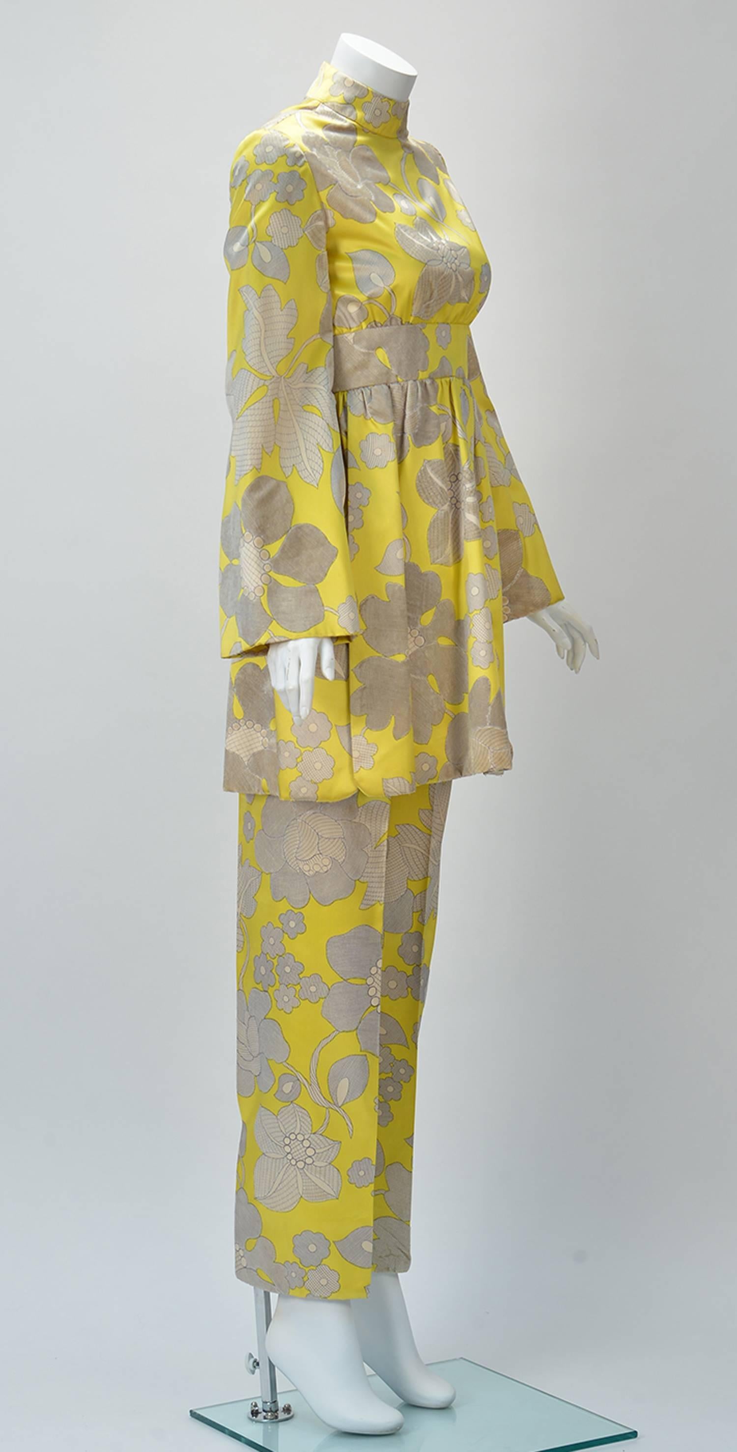 
One of a kind 1960's George Halley tunic and pant set. Tunic is yellow with grey and white flowers. Random velvet grey flowers throughout. Mock turtle neck, long bell sleeves, Defined empire waistband with gathers. Two slits on the side of the