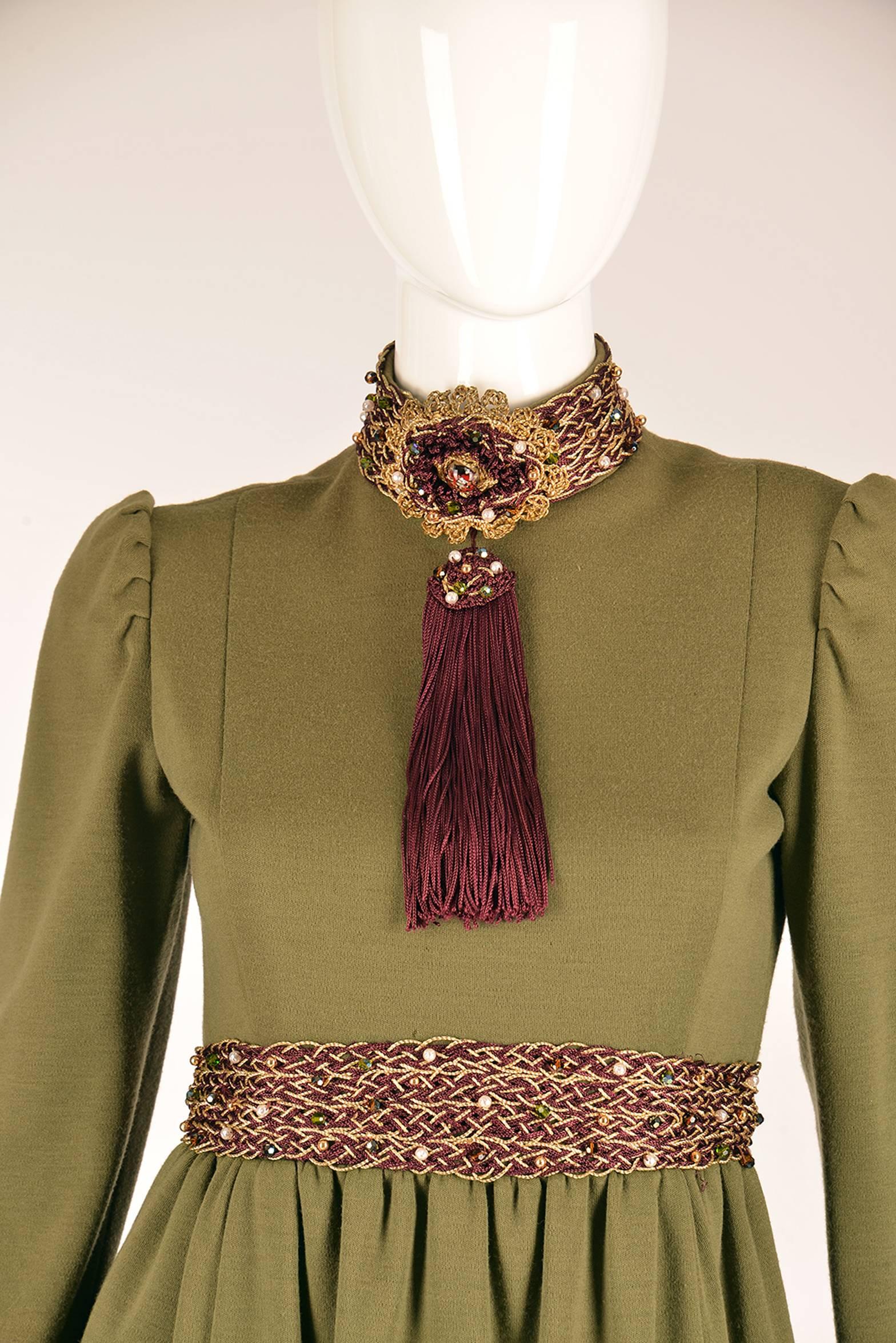 Late 1960s Geoffrey Beene olive green dress. High neck, long sleeves, and plum and gold braided thread looped together to form a chain around the neck, wrist, and waist. Three braids in total on the neck, wrist, and waist. Beading throughout the