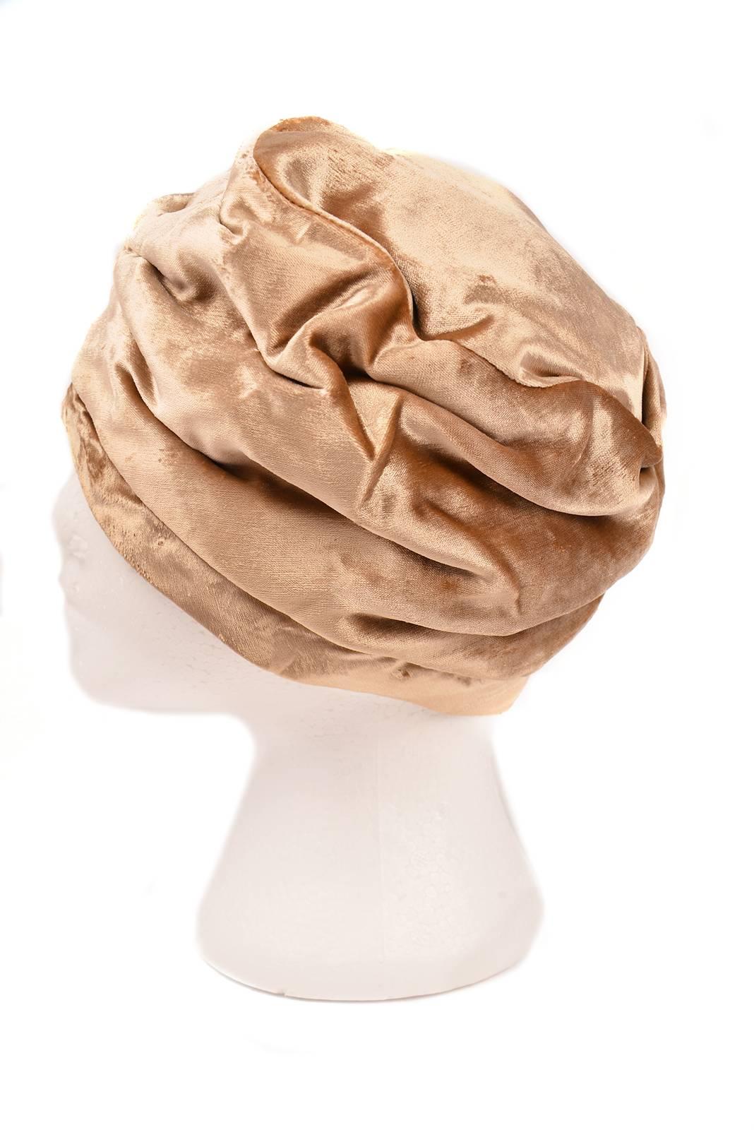 
Glamorous 1960s Mr. John turban style hat. This beautiful vintage hat is composed of champagne velvet folded into a undulating, organic, turban shape. The soft, wave-like construction of the hat pleats lend to its luxurious appearance. The hat is