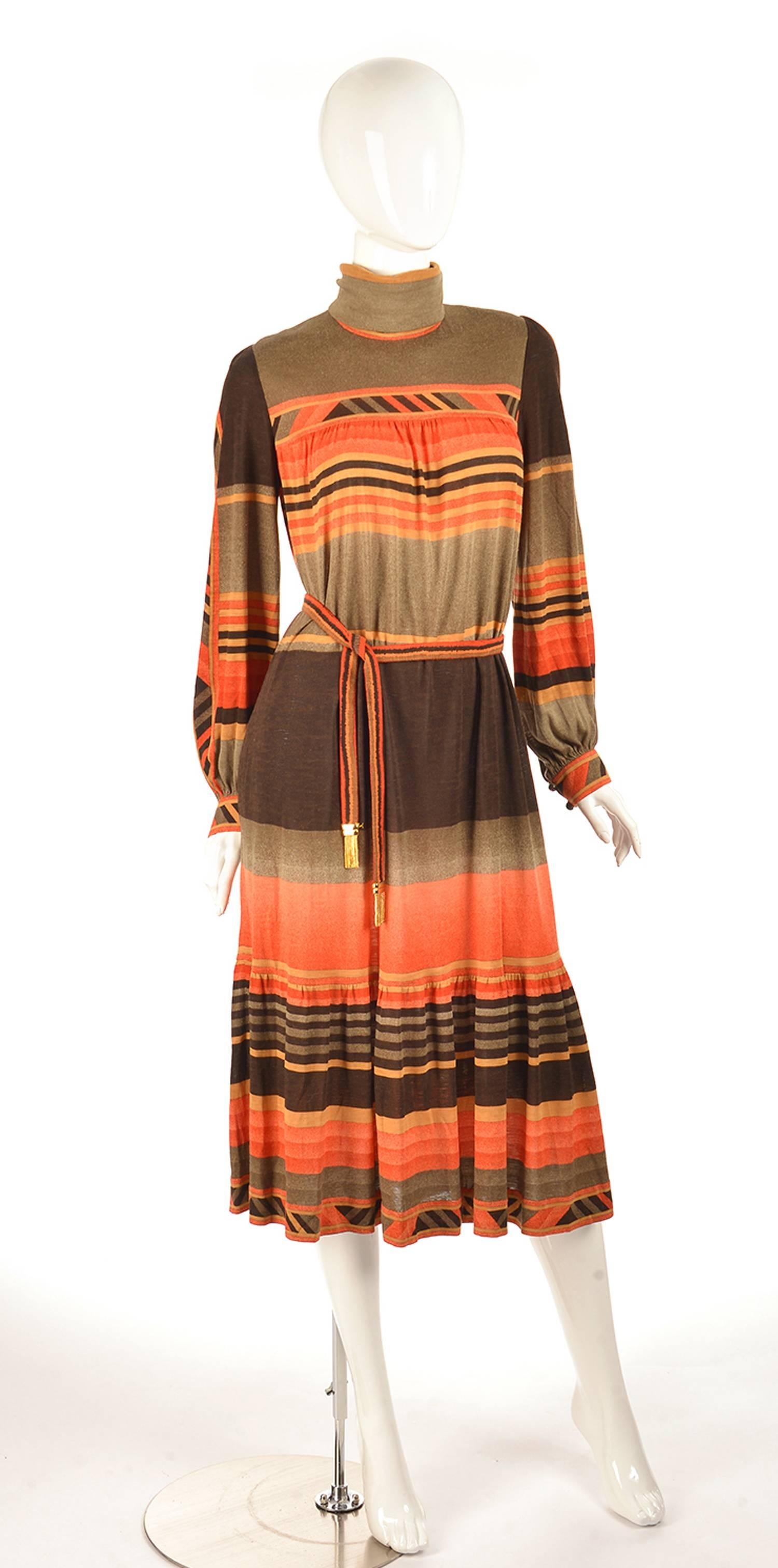 This light and breezy dress by Leonard Fashion Paris features a geometric stripe and triangle print. The dress has a turtleneck collar, cuff sleeves with brown and orange buttons, and a trumpet skirt. The belt has the same geometric print on it, as