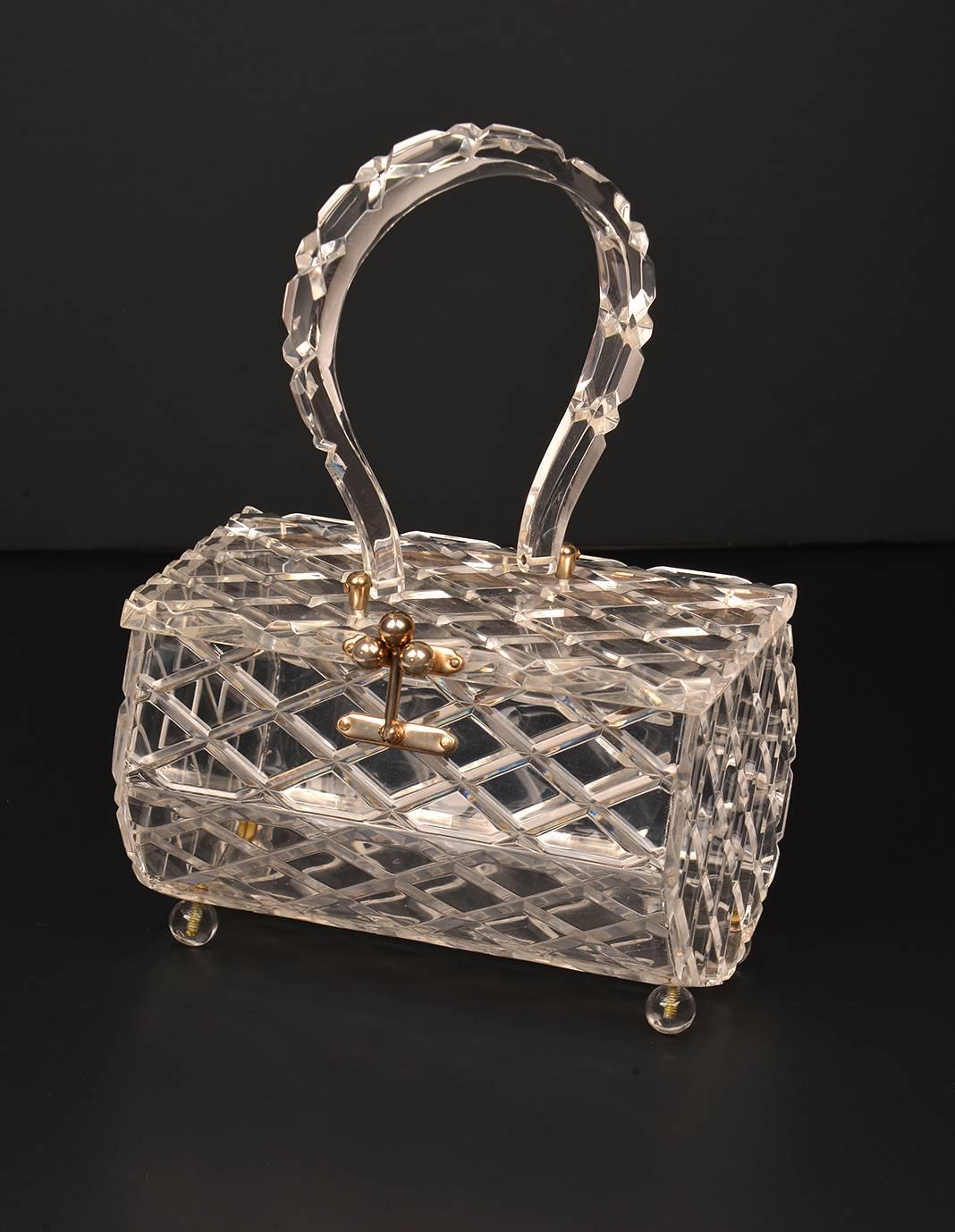Exquisite crystal clear 1950s Lucite top handle evening bag. The handbag features a crisp molded diamond lattice quilted pattern on the body, handle, and lid. The body of the purse is an elongated 7-sided heptagonal cylinder, and is supported on the