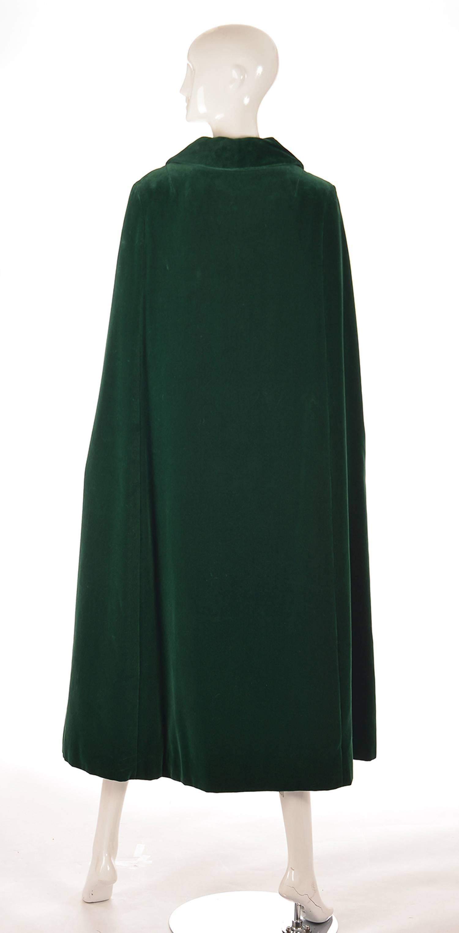 
This sumptuous, emerald green, velvet cloak is calf length, and features a long collar that can be turned up and held with a black carved glass button. The cloak features three large buttons composed of a cluster of green rhinestones Richard Kerr