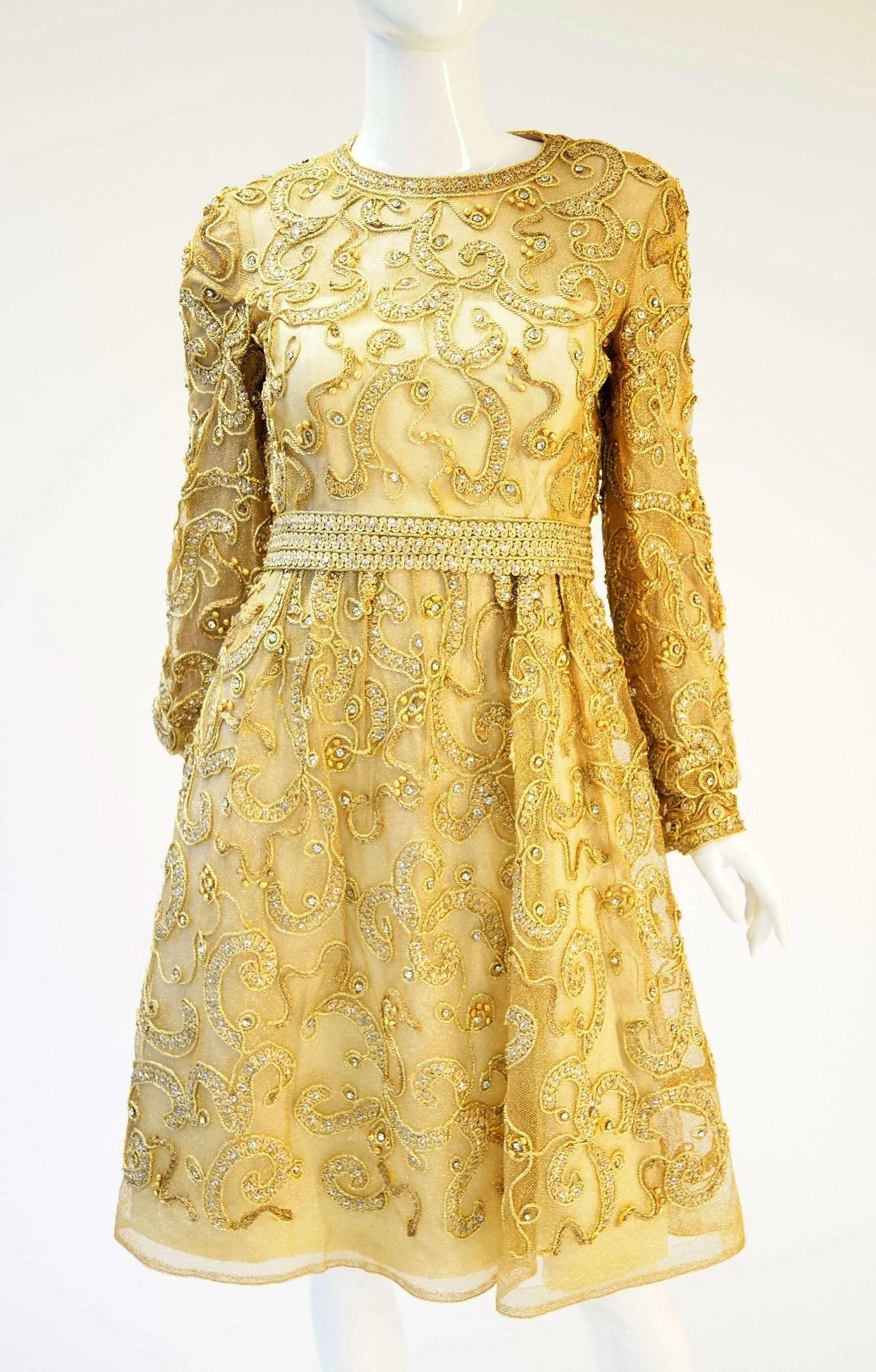Gorgeous 1960s dress by Malcolm Starr. This gorgeous cocktail dress is knee length, with long, cuffed sleeves, and jewel neckline. The dress features a delicate abstract floral design in gold embroidered passementerie, with rhinestone, sequin, and